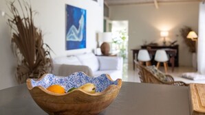 En träskål med frukt står på ett bord i ett väl upplyst rum med modern inredning, inklusive en soffa och stolar.