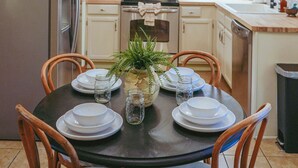 A modern kitchen with white cabinets, stainless steel appliances, and a dining table set for four. - 5 Minutes To Dollywood - Cottage With Fire Pit, Coffee Bar & Private Deck (Pigeon Forge)