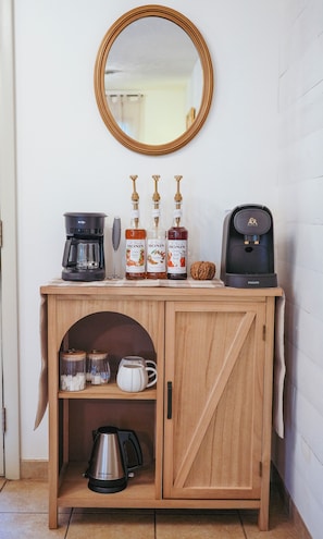 Un meuble en bois contenant une machine à café, trois bouteilles de sirop Monin, une cafetière et une bouilloire.