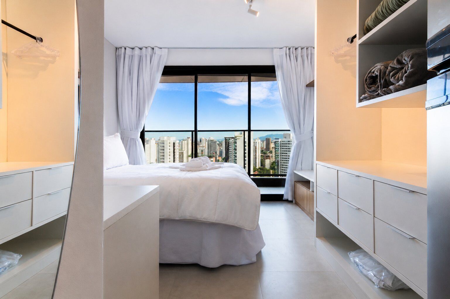Une chambre moderne avec un grand lit, des rideaux blancs, une vue sur la ville et un balcon.