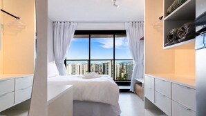 Un dormitorio moderno con una cama grande, cortinas blancas, vistas a la ciudad y un balcón.