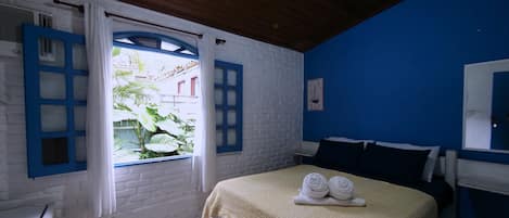 A room with a bed, a window with curtains, a blue wall, and a white brick wall.