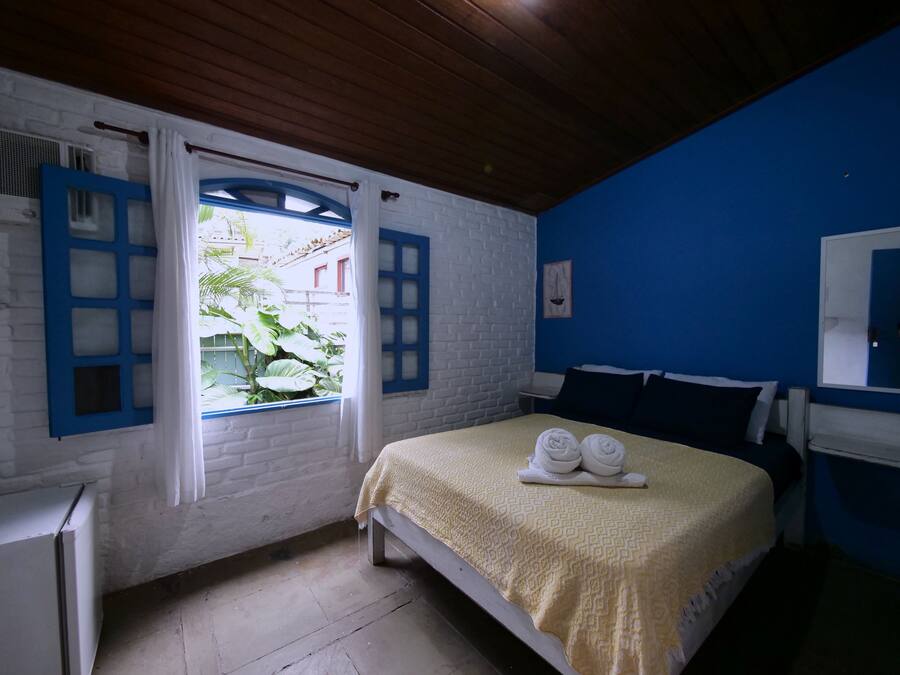 A room with a bed, a window with curtains, a blue wall, and a white brick wall.