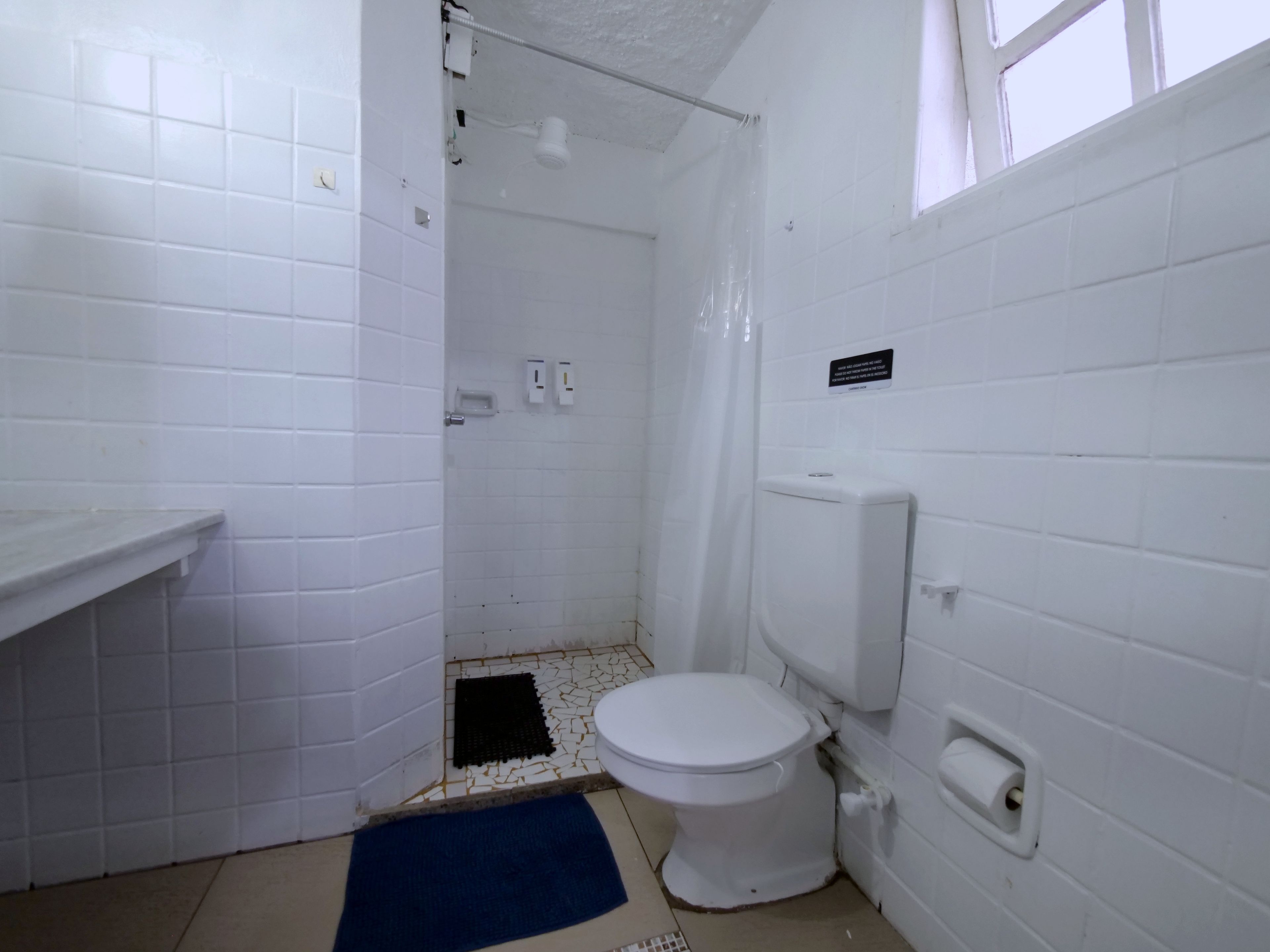 A small, white-walled bathroom with a toilet, a shower area, and a sink.