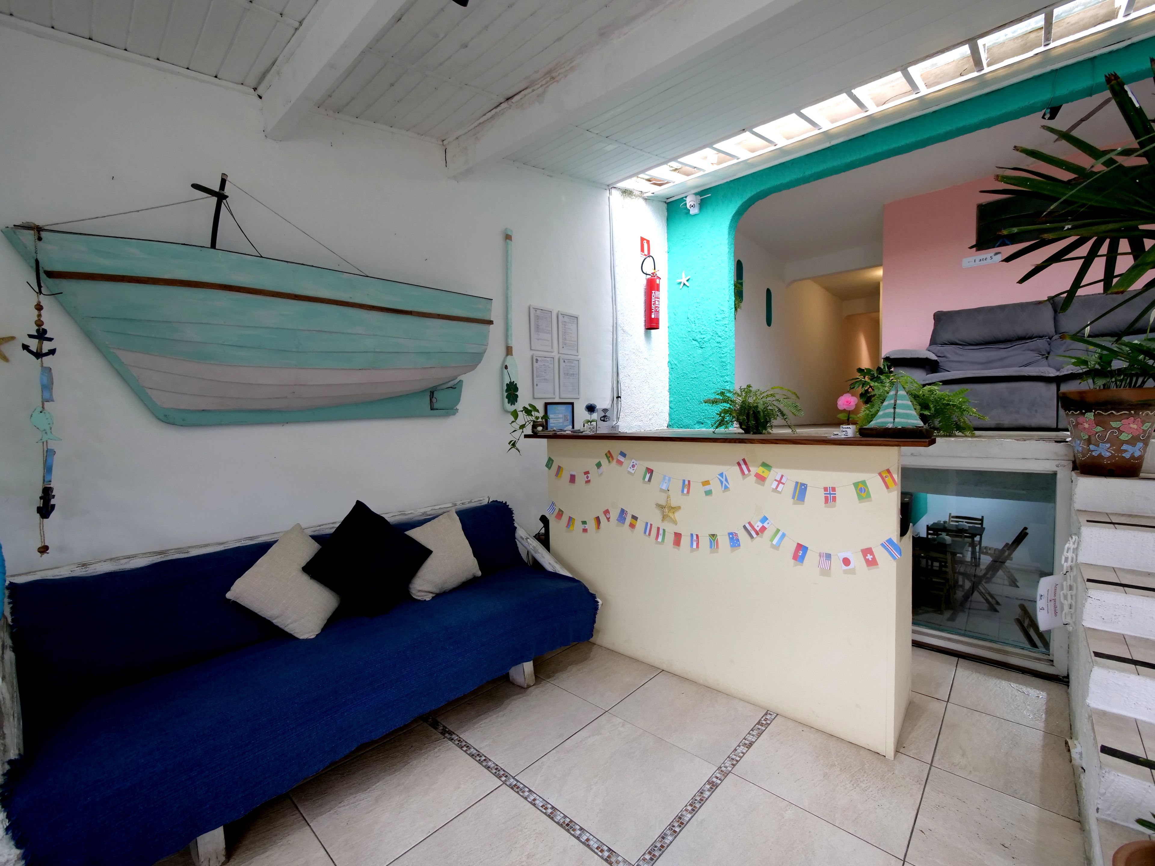 Una habitación con un sofá azul, un escritorio pequeño, un adorno de barco colgante y una planta en maceta.