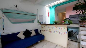 Una habitación con un sofá azul, un escritorio pequeño, un adorno de barco colgante y una planta en maceta.