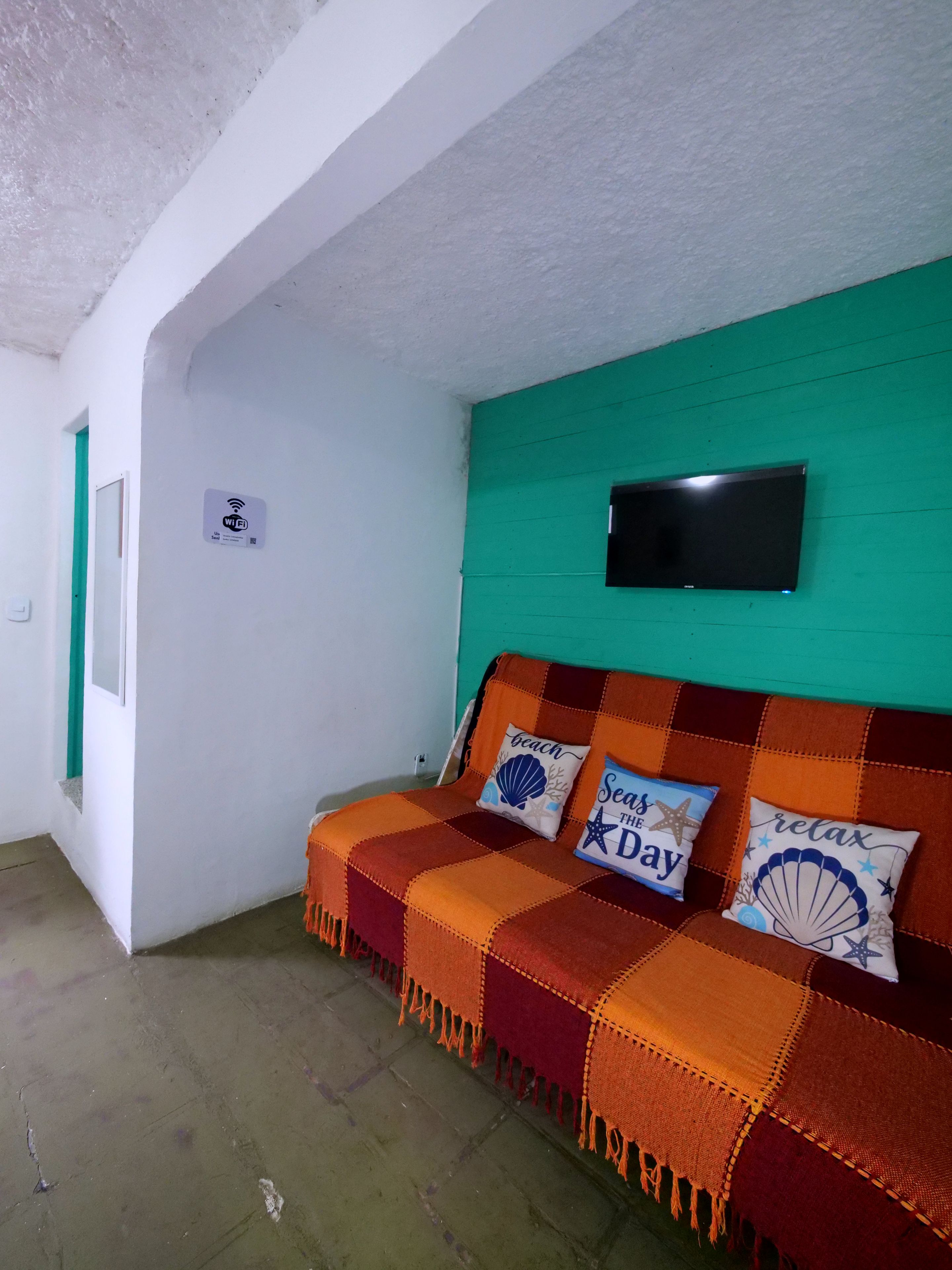 A room with a green wall, a television mounted above a sofa, and a WiFi sign on the wall.
