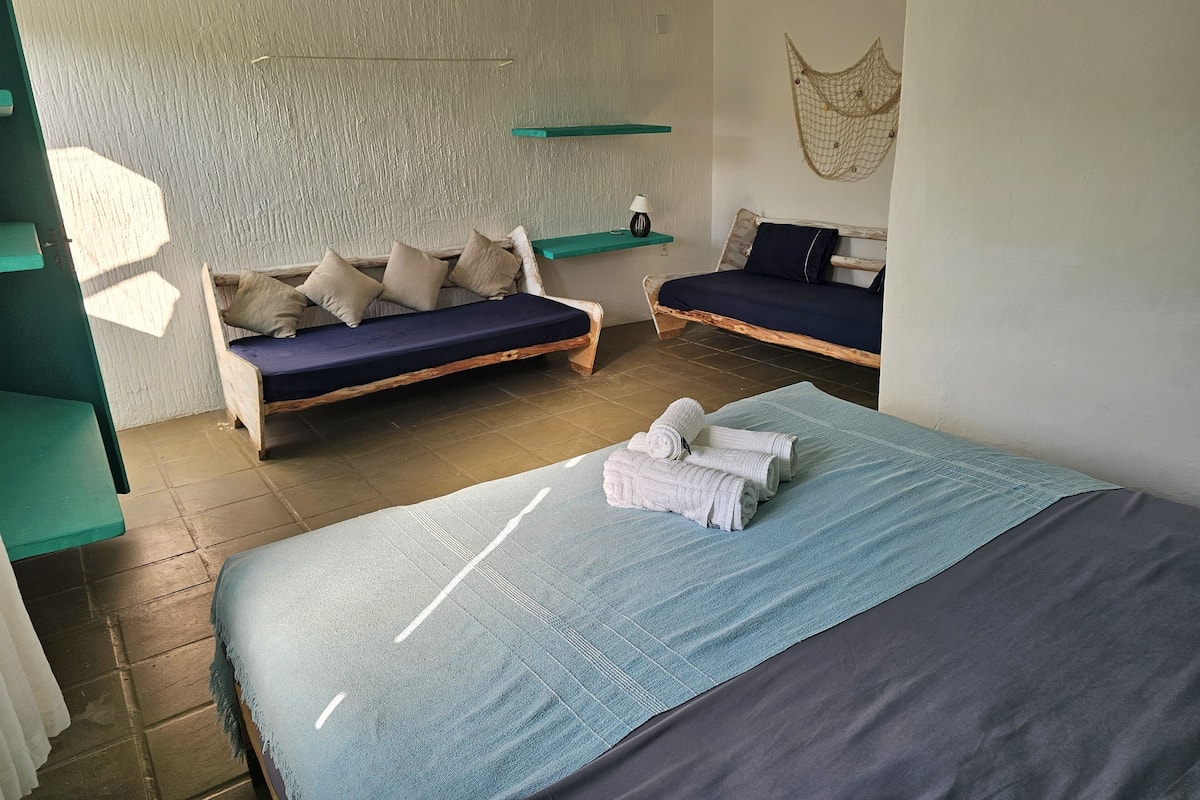 Ein Zimmer mit zwei Betten, einer hölzernen Bank, einem kleinen Regal und einem an der Wand befestigten Netz.