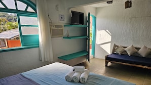 A room with a bed, a bench with pillows, a TV, and a window with curtains. - Pousada Canoa do Mar (Buzios)