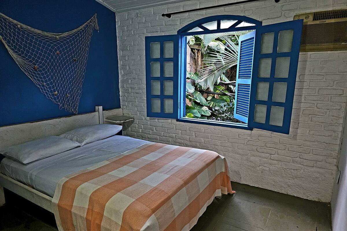Ein Bett mit gestreifter Decke, eine Hängematte und ein Fenster mit blauen Fensterläden.
