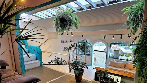 A spacious indoor area with a high ceiling, a blue staircase, and multiple potted plants. - Pousada Canoa do Mar (Buzios)