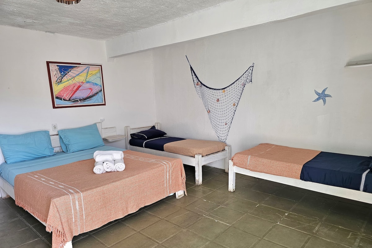 Ein Zimmer mit zwei Einzelbetten, einem kleinen Tisch, einem Stuhl, einer Hängematte und einer Meeressstern-Dekoration.