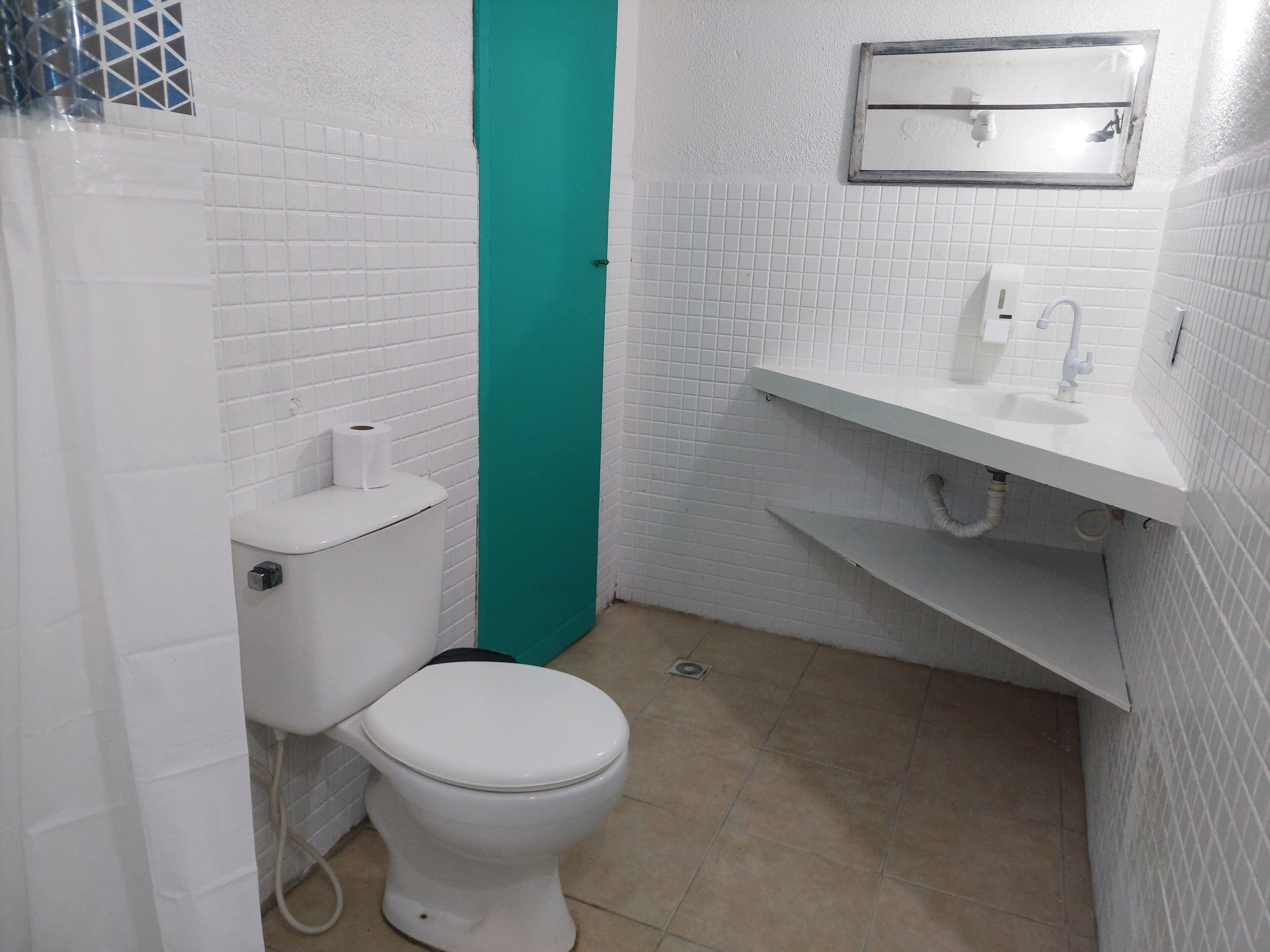 A small, clean bathroom with white tiled walls, a white toilet, a green door, and a white sink with a mirror above it.
