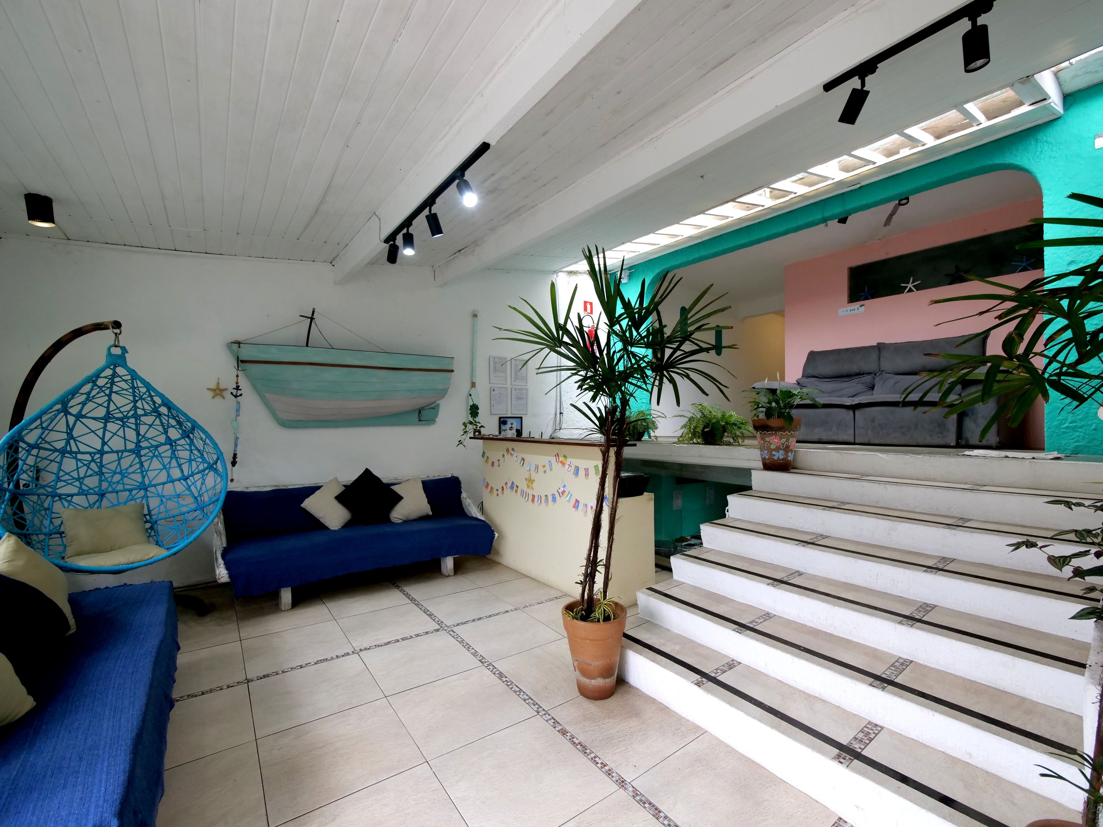 A living room with a blue sofa, a hanging chair, a staircase, and a potted plant.