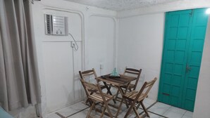 A room with a tiled floor, a wooden dining table with four chairs, a teal door, and a white wall with a power outlet. - Pousada Canoa do Mar (Buzios)
