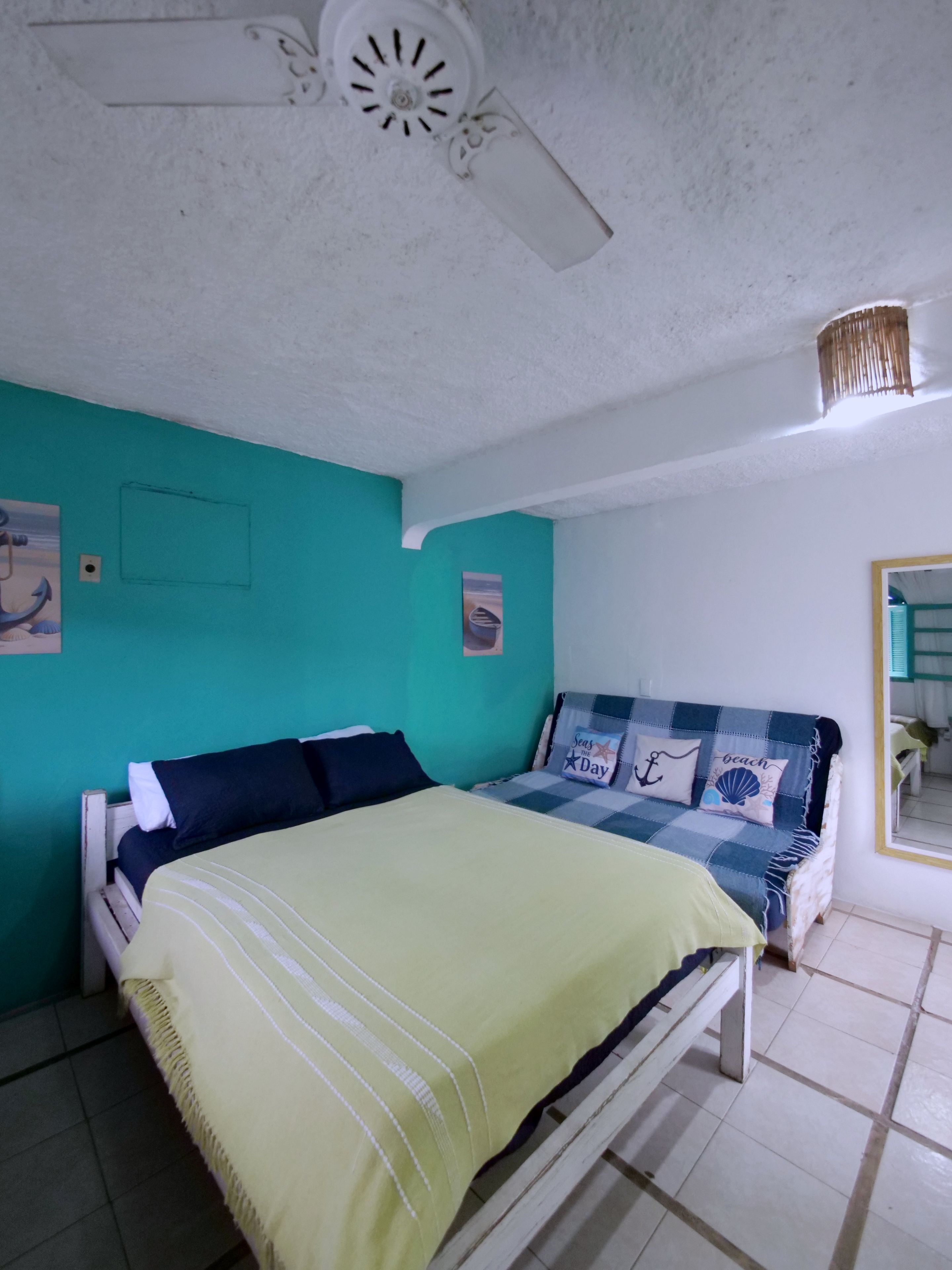 Une chambre à coucher avec un lit, un ventilateur de plafond, un luminaire fixé au mur et une fenêtre avec des rideaux.