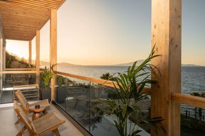 Un área de estar moderna al aire libre con mobiliario de mimbre, barandilla de cristal y vista al mar.