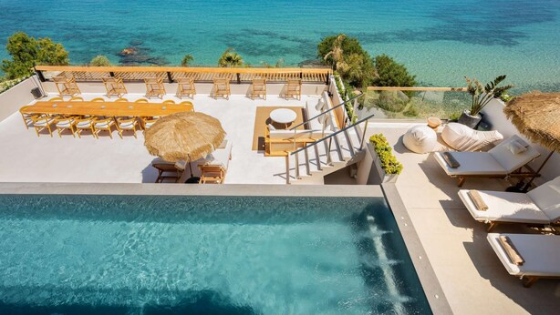 A rooftop pool area with lounge chairs, a dining table, and a staircase leading to a balcony overlooking the sea. - Residence Callisto Azzure (Tragaki)
