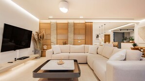 A modern living room with a sectional sofa, a coffee table, and a flat-screen TV. - Residence Callisto Azzure (Tragaki)