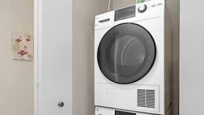 A compact, white stacked washer and dryer unit in a small room with a light-colored wall and a wooden floor. - Comfortable 2BR ! Free parking ! 30 min to NYC ! (Newark)