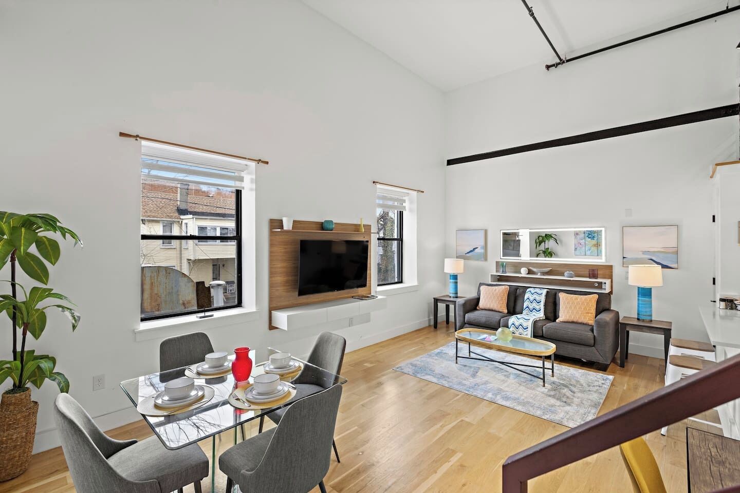 A modern living room with a flat-screen TV, a dining area with a glass table, and a staircase leading to another level.