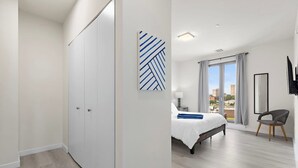 A modern hotel room with a large bed, a wardrobe, a view of the city, and a flat-screen TV.