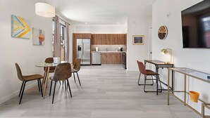 A modern kitchen with wooden cabinets, a stainless steel refrigerator, and a dining area with a glass table and chairs.