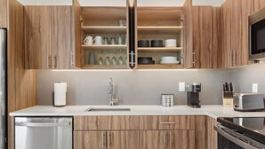 A modern kitchen with wooden cabinets, a stainless steel dishwasher, a built-in oven, a coffee maker, and a toaster.