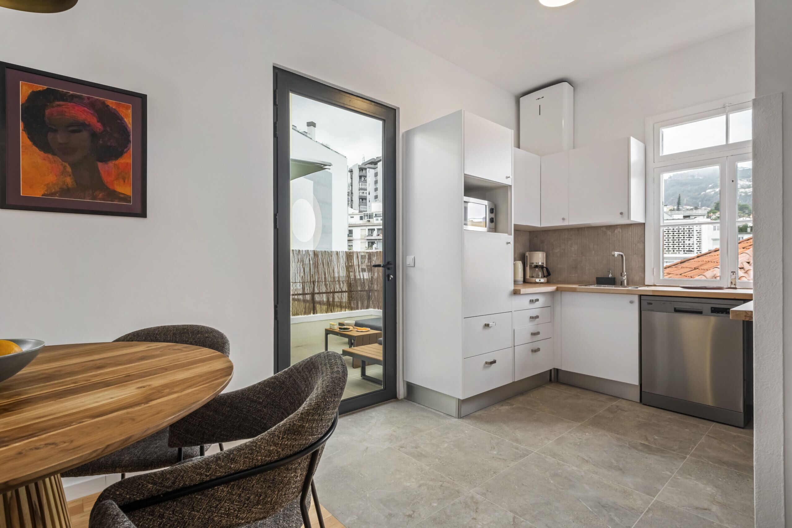 A modern kitchen with white cabinets, a stainless steel dishwasher, and a dining area with a wooden table and two chairs.