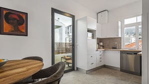 A modern kitchen with white cabinets, a stainless steel dishwasher, and a dining area with a wooden table and two chairs. - The Graceful Manor by Homie (Funchal)