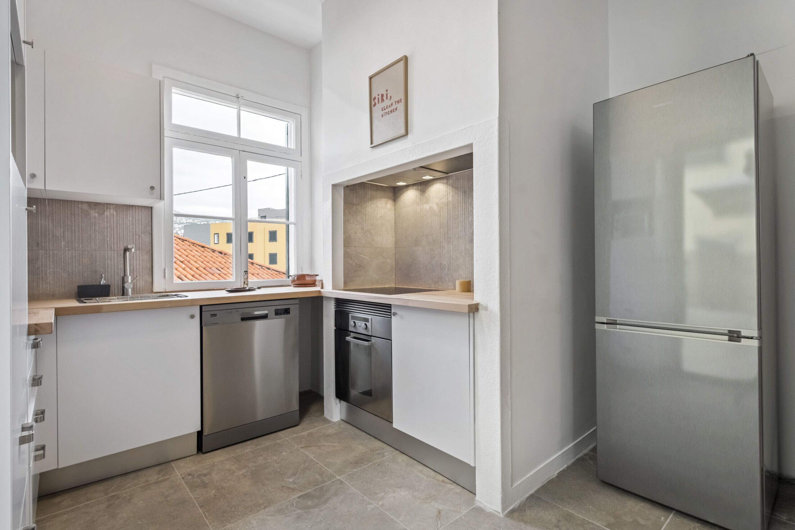 Una cocina moderna con armarios blancos, un refrigerador de acero inoxidable y una ventana con vista a un edificio.