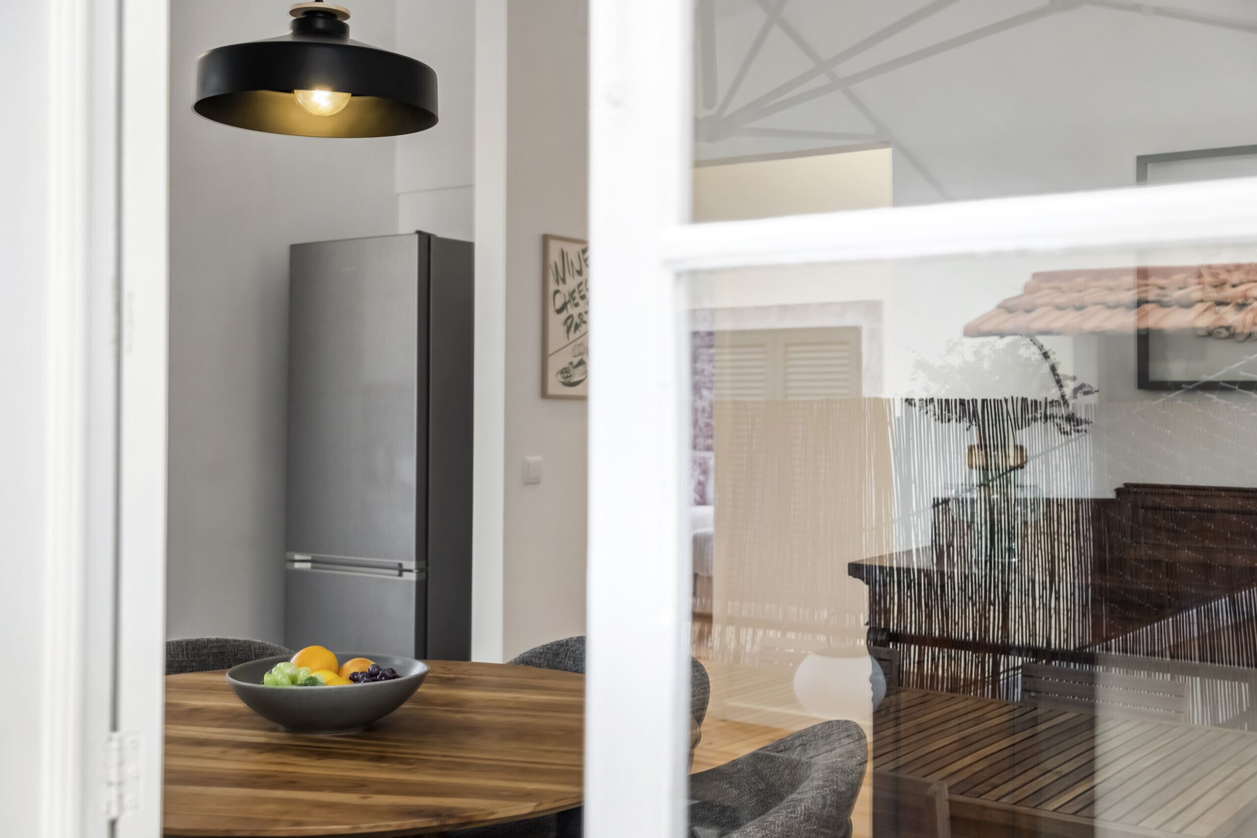 A modern kitchen with a wooden dining table, a bowl of fruit, and a tall appliance.
