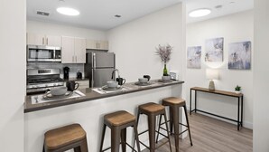 Une cuisine moderne dotée d’appareils électroménagers en acier inoxydable, d’un coin bar avec des tabourets et d’un décor minimaliste.