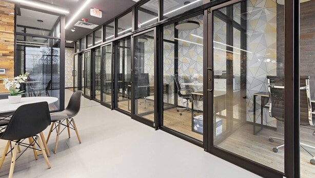 Un espacio de oficina moderno con divisiones de vidrio, una mesa redonda con sillas y una silla de oficina visible.