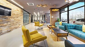 Un espacio de oficina moderno con pared de piedra, muebles amarillos y azules, un televisor y ventanas amplias.