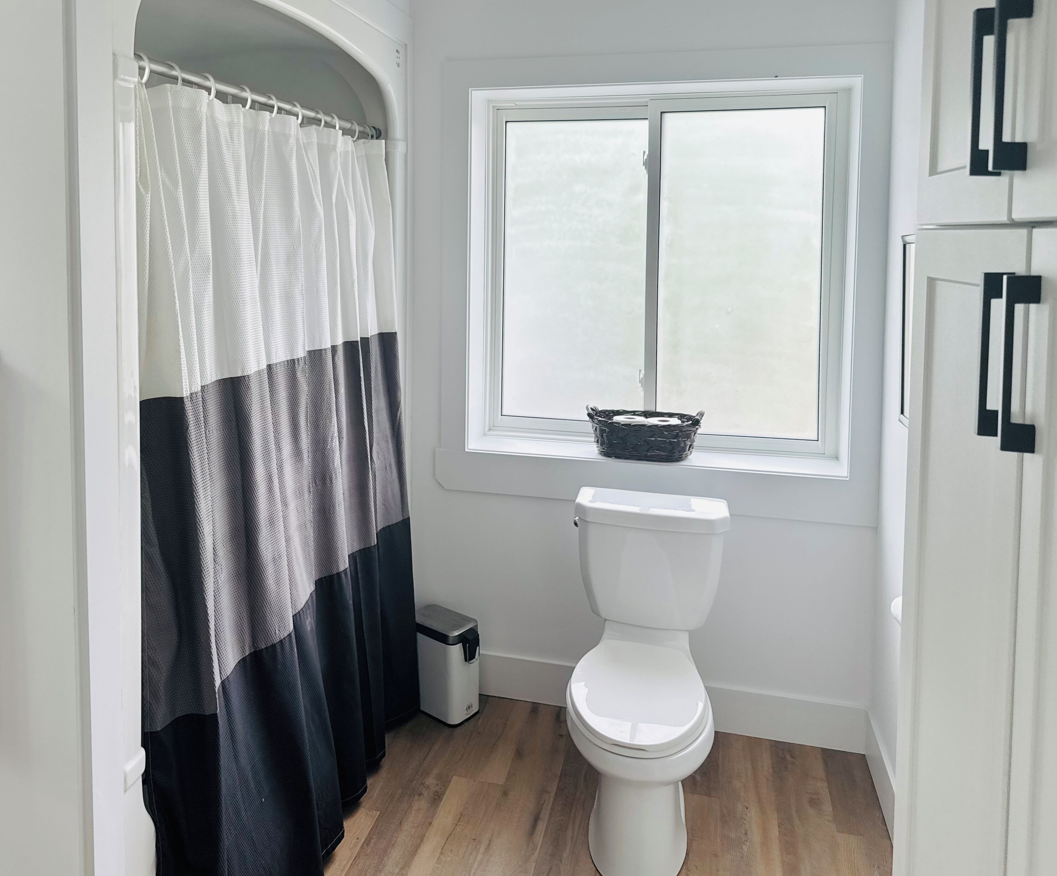 A bathroom with a toilet, a window with a basket on the sill, and a shower curtain.