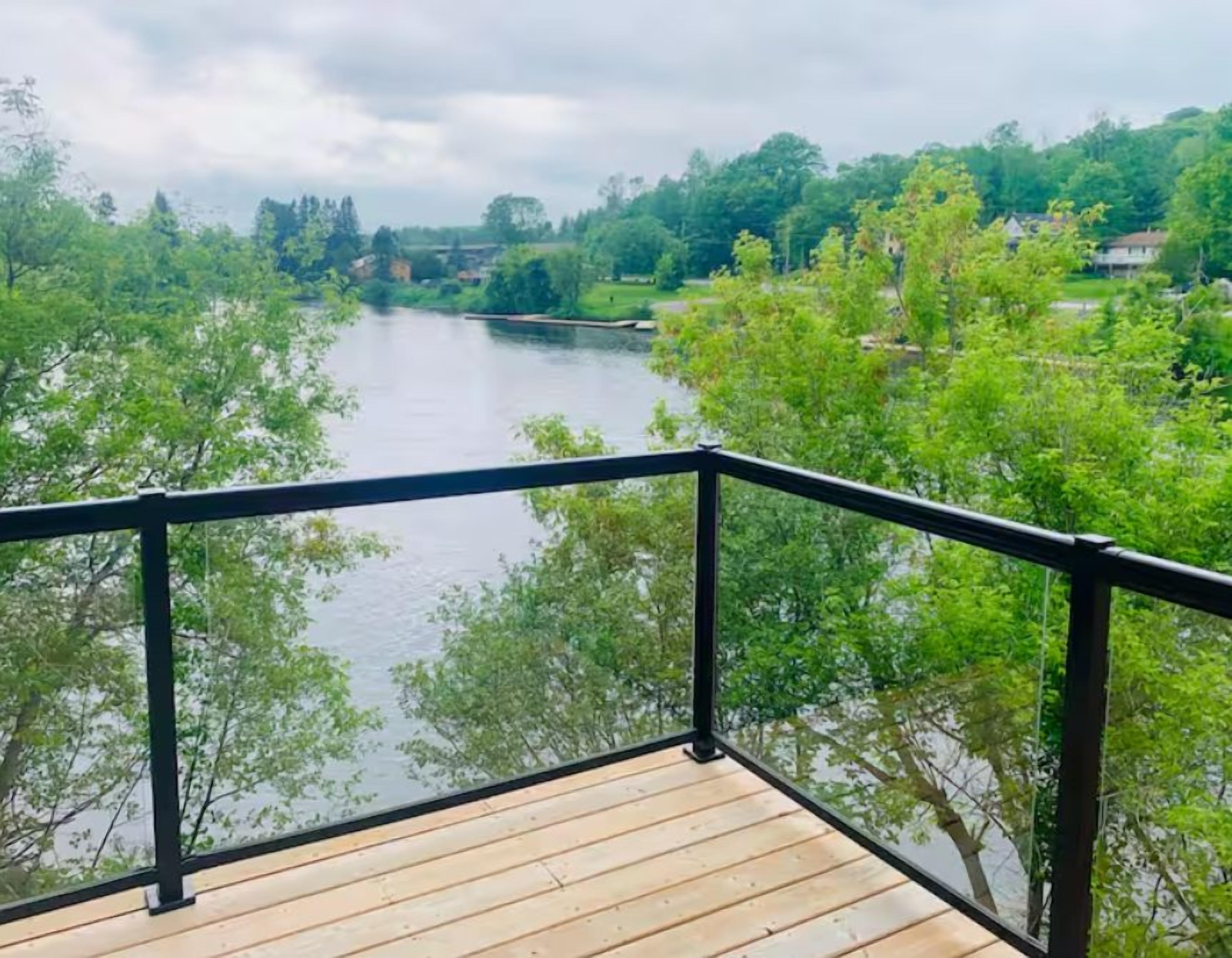 A wooden deck with a black railing overlooking a river surrounded by trees.