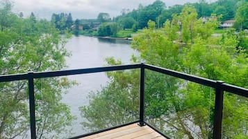 A wooden deck with a black railing overlooking a river surrounded by trees.