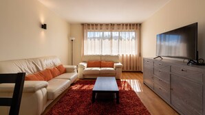Ein Wohnzimmer mit einem beigen Sofa, einem passenden Sessel, einem Couchtisch und einem Fernseher auf einer Holzkommode.