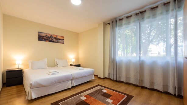 Ein Hotelzimmer mit zwei Betten, einem Nachttisch, einer Lampe, einem Bild an der Wand und einem Fenster mit Vorhängen.