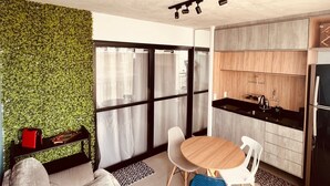 A modern living room with a green wall, a wooden dining table, and a kitchen area with wooden cabinets and a black countertop. - Vita 1409 Centro SP Bom Retiro - Digital Check-in with Wi-Fi (Bom Retiro São Paulo)