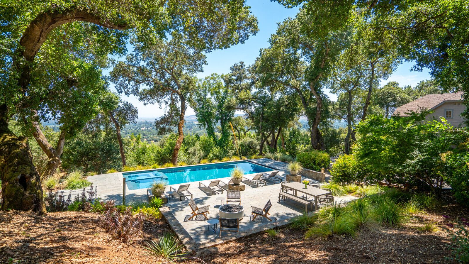 Una piscina con sillas de descanso y una mesa, rodeada de árboles y follaje.
