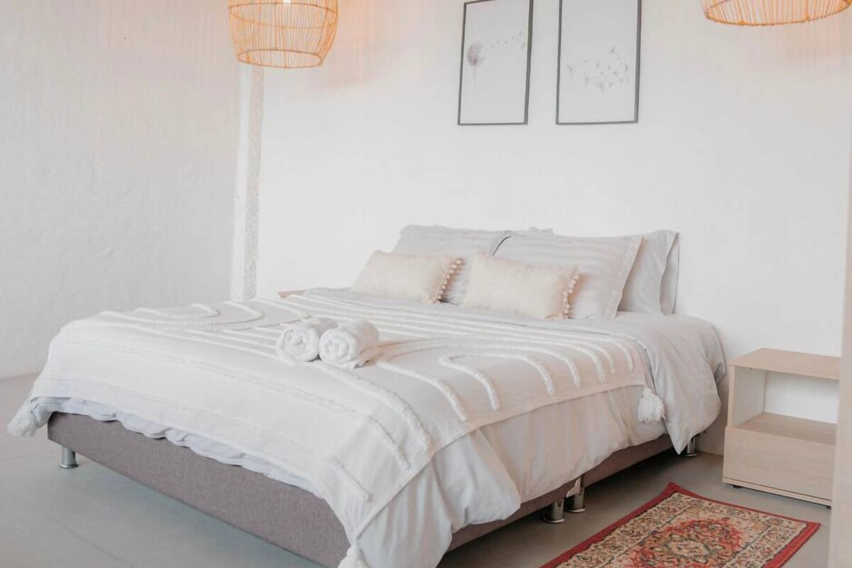 Ein schlicht eingerichtetes Schlafzimmer mit einem Bett, zwei an der Wand befestigten Bilderrahmen und zwei hängenden Lampen.