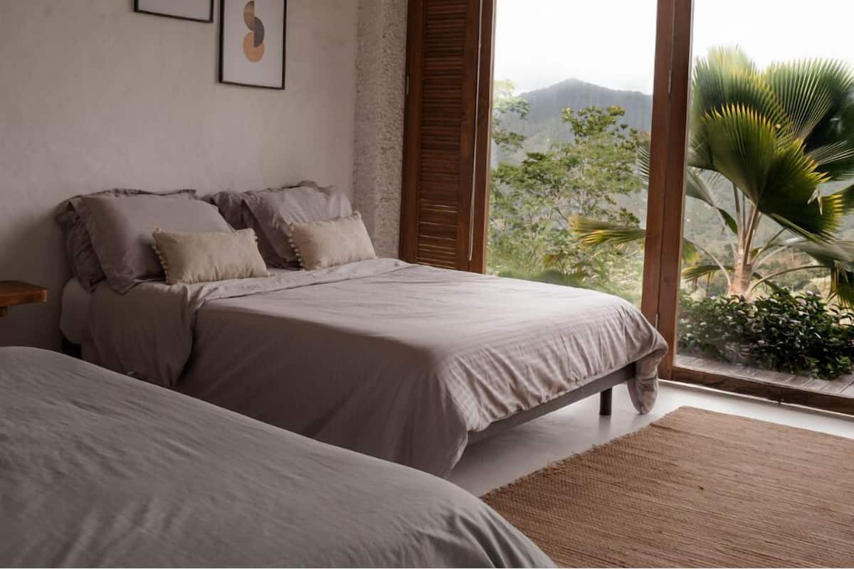 Ein Schlafzimmer mit einem großen Bett, einem kleineren Bett und einem Fenster mit Blick auf Grünflächen und Hügel.