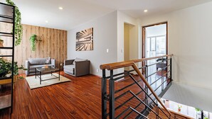 Een moderne woonkamer met houten vloeren, een trap met houten balustrade en een groot raam.