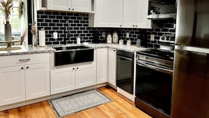 Una cocina moderna con armarios blancos, un salpicadero de baldosas negras, electrodomésticos de acero inoxidable y suelo de madera.