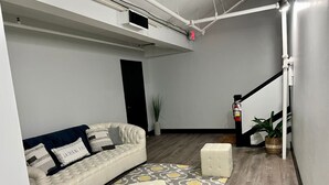 Una sala de estar moderna con un sofá, un reposapiés, una alfombra estampada y una escalera.