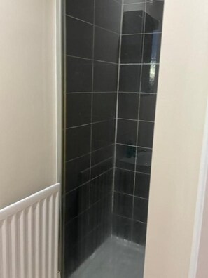 A narrow, tiled shower area with a white radiator on the left. - Komegloba Mega room (Manchester)