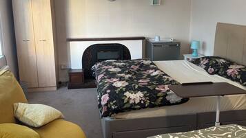 A hotel room with a bed, a small table, a wardrobe, a nightstand, a lamp, and a clock on the wall.