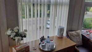 A hotel room with a wooden desk, a vase of white flowers, a tray with cups and a kettle, and a view of a road and greenery outside. - OYO Baytree Lodge (Bangor)